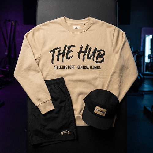 THE HUB Athletics Dept. sand crewneck, black coach shorts and cap